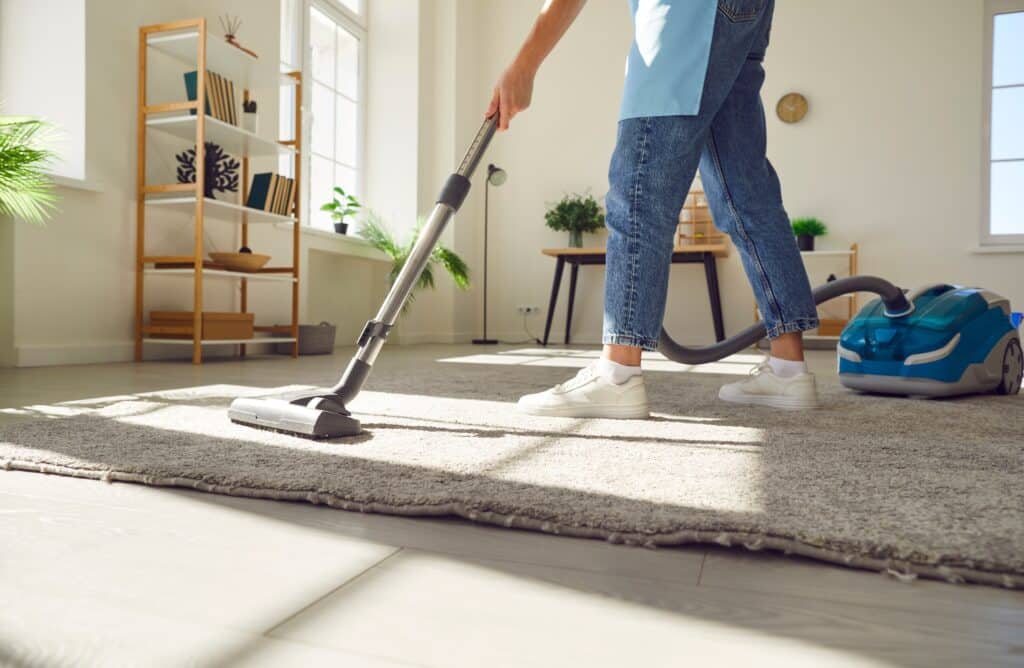 Nettoyage de tapis professionnel avec aspirateur à domicile Personne passant l'aspirateur sur un tapis gris dans un salon lumineux pour un nettoyage professionnel.